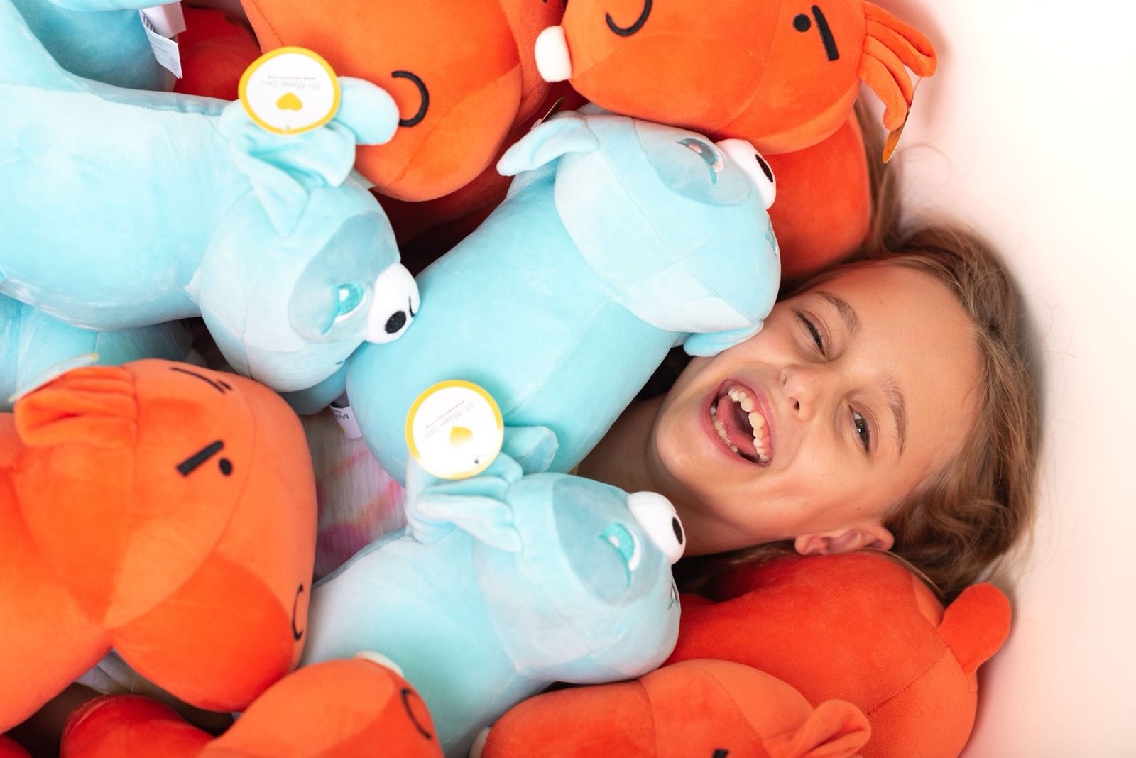 Girl laughing in a pile of My Mama Says plush friends