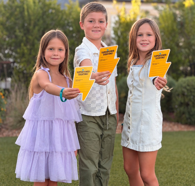 Three children outdoors holding yellow Superpower Sighting thunderbolt cards